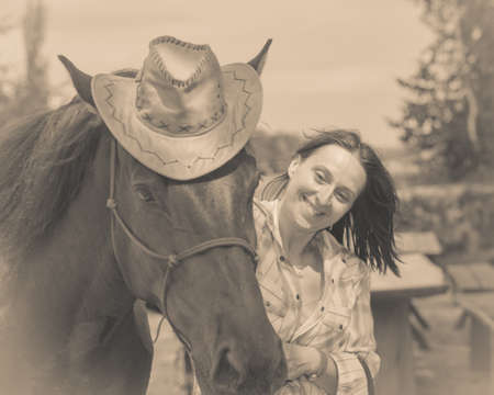 Fun with animals concept. Western redhead woman hugging horse wearing cowboy hatの写真素材