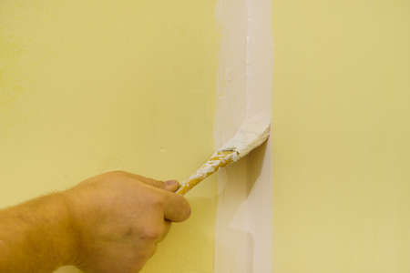 Person appplying white paint on yellow wall using brush. Home renovation concept.の写真素材