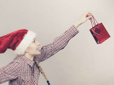 Xmas, seasonal clothing, winter christmas concept. Happy woman wearing windblown Santa Claus helper hat holding shopping bagの写真素材