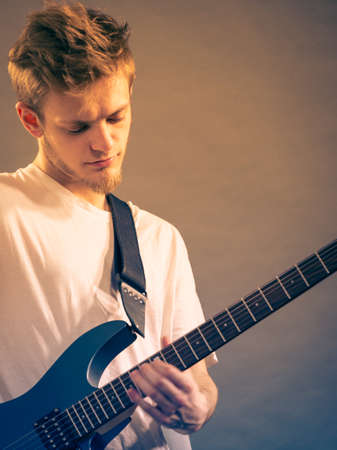 Young bearded man with electric guitar. Adult person is holding instrument and playing. Hobby, music concept, on greyの写真素材
