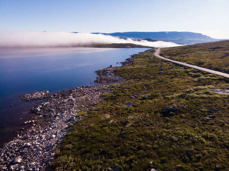 Aerial view. Road crossing Hardangervidda mountain plateau, clouds over lakes, morning time. Norway landscape. National tourist Hardangervidda route.の写真素材