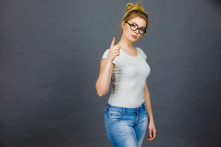 Young attractive woman wearing eyeglasses pointing into camera, teenage judging someone. Studio shot...