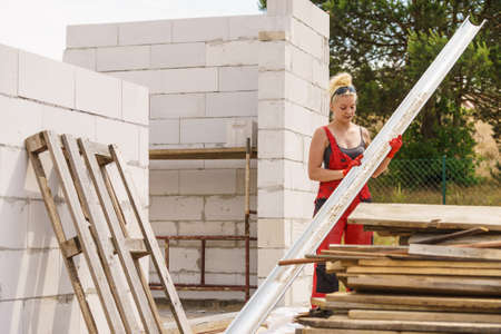 Woman carrying steel metal made gutter on her house construction site, building new home, fixing...