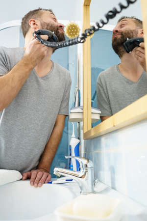 Bearded man looking at himself in mirror trimmng, shaving his beard using electric timmer razor.の写真素材