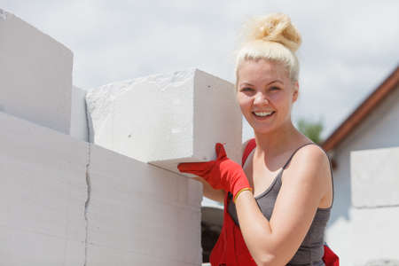 Strong pretty woman working on construction site, building house, installing gray airbricks. Industrial work concept.の写真素材