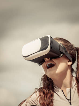 Young woman testing VR glasses outside. Female wearing virtual reality headset during summer weather