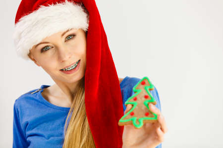 Smiling young woman holding little christmas tree made of sweet gingerbread cookie.の写真素材