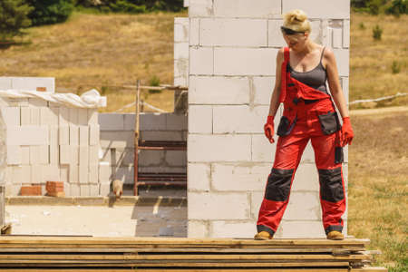 Blonde strong woman in dungarees working on home construction site. Women power, gender equality, industrial worker.の写真素材