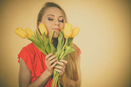 Lovely young woman long blonde hair holding smelling yellow tulips.の写真素材