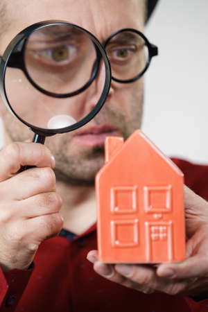 Funny looking adult man examining red model home using a magnifying glass, house inspection and real estate conceptの写真素材