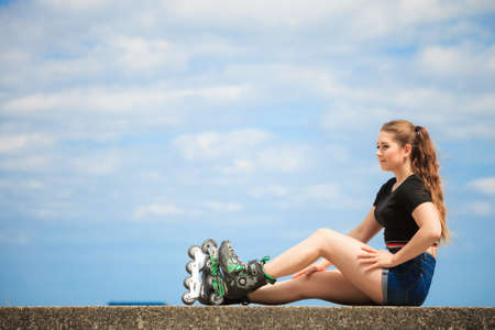 Happy joyful young woman wearing roller skates relaxing after long ride. Female being sporty having fun during summer time near sea.の写真素材