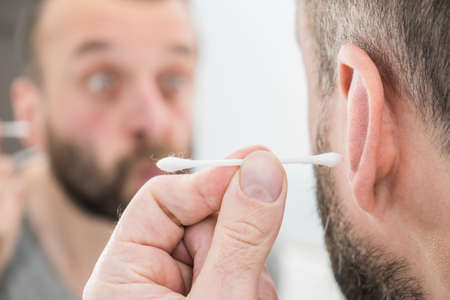 Man about to clean his ears using Q-tip cotton swab. Hygiene essentials concept. Removing wax from ear.の写真素材