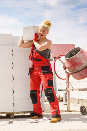 Strong pretty woman working on construction site, building house, installing gray airbricks....