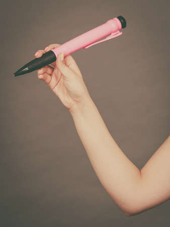 Unrecognizable woman hand holding big pen. Studio shot on dark grey background.の写真素材