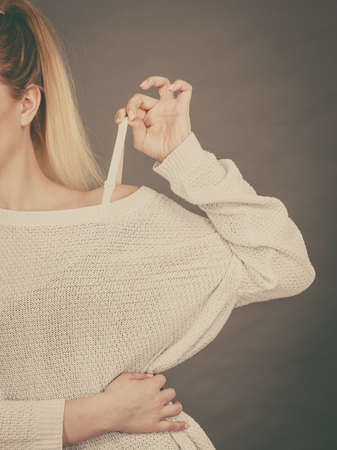 Woman holding her bra strap from under her sweater. Brafitting concept. Grey background.の写真素材