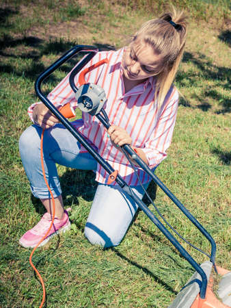 Female person mowing green lawn with lawnmower in sunny day.