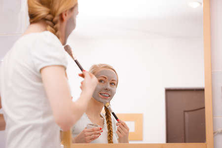 Blonde woman in bathroom with gray clay mud mask on her face.の写真素材