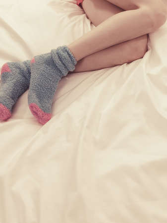 Woman lying on bed wearing warm furry socks only. Sleepwear accessories concept.