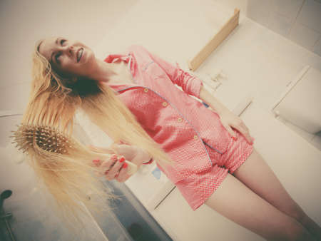 Woman wearing pajamas in bathroom having fun while brushing her long blonde hair, windblown hairdo, shot from bottom.の写真素材