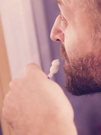 Adult man brushing his teeth looking at his bathroom mirror during morning hygiene routine.の写真素材