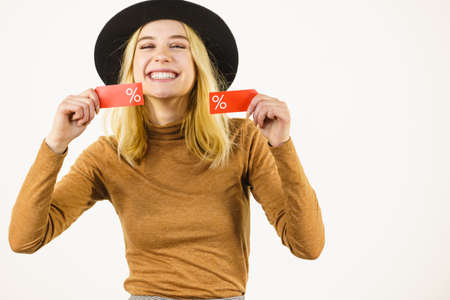 Woman in hat showing tag with shopping sale percentage sign enjoying cheap clothing. Female wearing stylish outfit.の写真素材