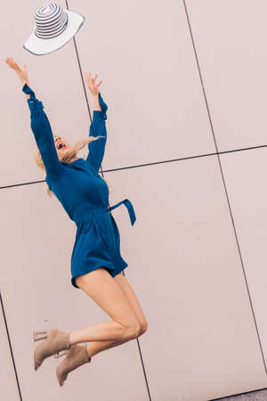 Happy joyful woman wearing blue jumpsuit having fun throwing her sun hat. Fashion model and summer outfit.の写真素材