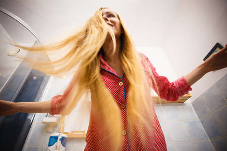 Woman wearing pajamas in bathroom having fun while brushing her long blonde hair, unusual shot from bottom.の写真素材