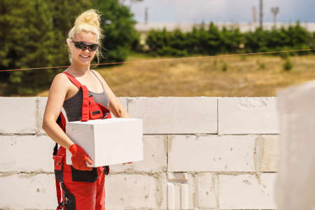 Strong pretty woman working on construction site, building house, installing gray airbricks....