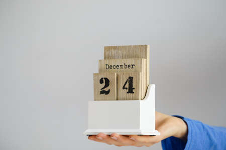 Woman hand holding wooden calendar with christmas 24 december date. Seasonal holiday concept.の写真素材