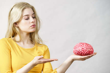 Serious teenage woman holding fake brain having something on mind, thinking of solution idea.の写真素材