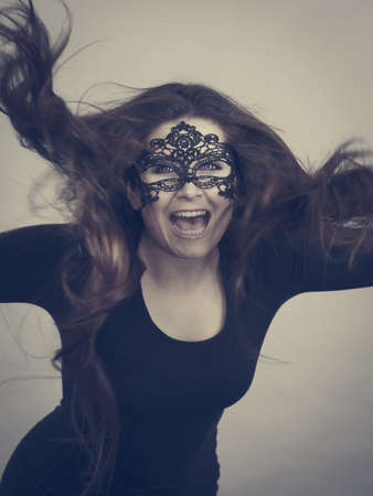 Happy pretty mysterious woman wearing black eye lace mask having tousled windblown long brown hair.
