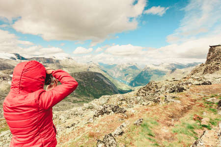 Female tourist taking photo with camera, enjoying Geirangerfjord and mountains landscape from...