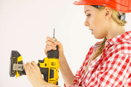 Woman wearing helmet using drill. Girl working at flat remodeling. Building, repair and renovation.