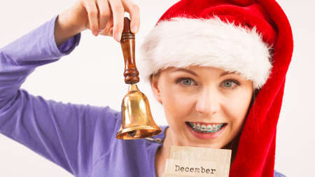 Happy positive young teenage woman wearing Santa Claus christmas hat holding calendar with 24 december date and bellの写真素材