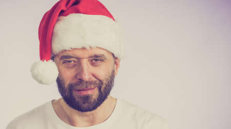 Bearded man wearing santa claus hat portrait, on grey with copy space. Christmes time.の写真素材