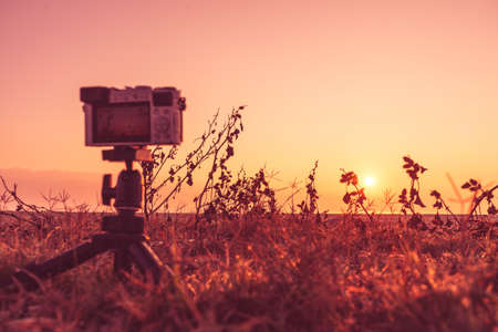 Professional camera on tripod taking picture film video of sunrise over sea surface, Greece