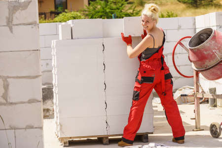 Strong pretty woman working on construction site, building house, installing gray airbricks. Industrial work concept.の写真素材