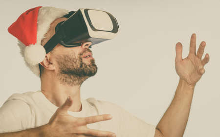 Man wearing santa claus hat exploring space with virtual reality goggles headset, vr box. Cyber...