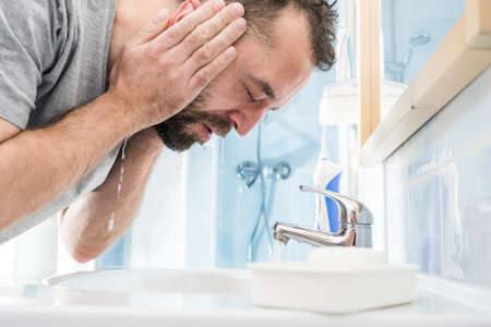 Man splashing water on his face, washing himself, taking care of personal hygiene. Feeling fresh in the morningの写真素材