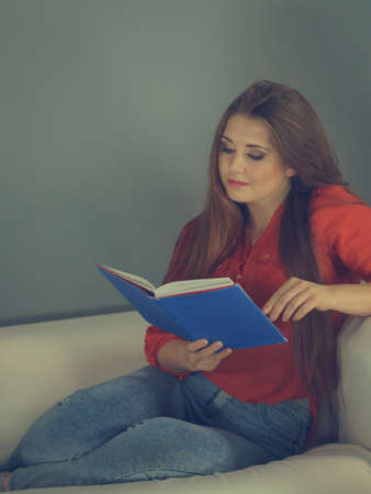 Woman enjoying her leisure time relaxing while reading interesting book sitting on sofa. Relaxation...