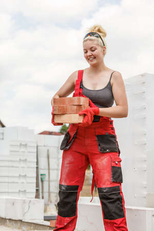 Strong pretty woman working on construction site, building house, installing bricks. Industrial work...