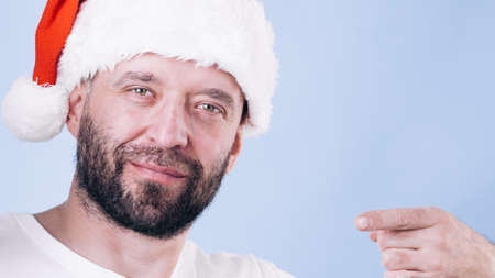 Christmas man wearing santa claus hat pointing with finger at you, on blueの写真素材