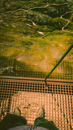 Tourist feet on Dalsnibba viewpoint, Geiranger Skywalk platform metal floor surface and view on mountains landscape, Norway.の写真素材