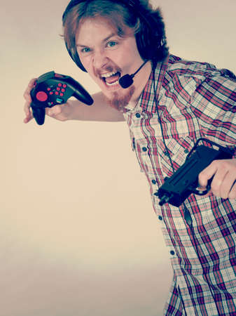 Nerd geek young adult man playing on the video console holding gun wearing headphones with microphone. Gaming gamers concept.の写真素材