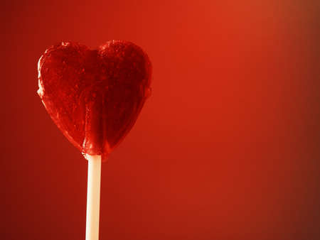 Sweet candy heart on stick against red background. Love, valentines day or charity concept.の写真素材