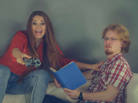 Couple sitting on couch spending free time. Woman playing video games and man reading book.の写真素材