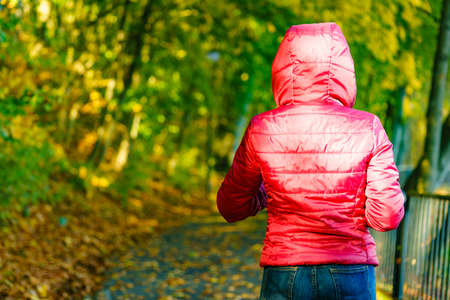 Unrecognizable woman having nice autumn walk during warm weather in park. Female wearing red...