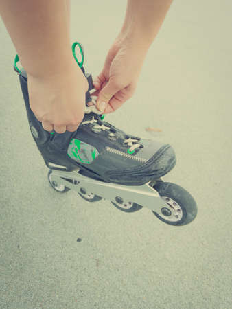 Unrecognizable woman putting on roller skates. Female being sporty having fun during summer in city