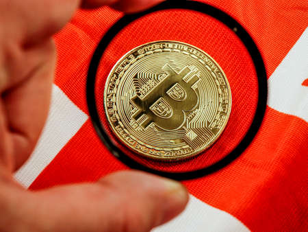 Male's hand holding magnifying glass looking on new virtual money btc bitcoin placed on British...