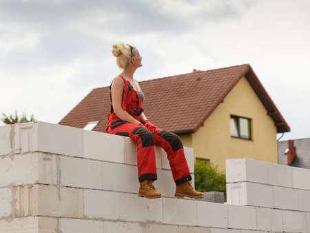 Blonde woman wearing dungarees relaxing after hard work on construction site. Female taking break dreaming of building her home.の写真素材